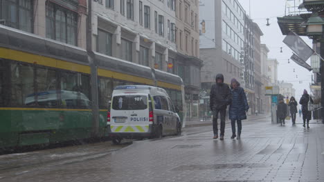 Tram,-police-car-and-people-with-masks-on-central-street-of-a-big-city-on-a-cold-and-snowy-winter-day-during-covid-pandemic