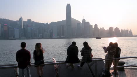 Paare-Versammeln-Sich-Entlang-Der-Uferpromenade-Von-Victoria-Harbour,-Während-Sie-Den-Blick-Auf-Die-Skyline-Der-Insel-Hongkong-Genießen,-Während-Der-Sonnenuntergang-Einsetzt