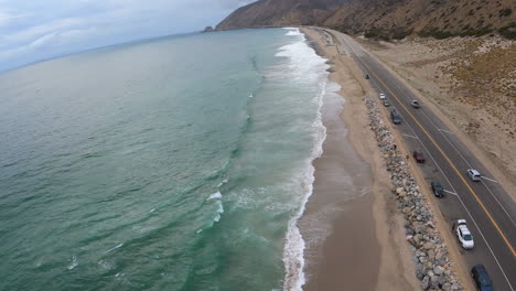 Drone-Shot-over-Pacific-Coast-Highway,-Crashing-Ocean-Waves-and-Majestic-Mountains