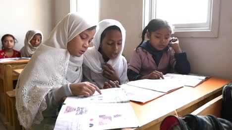 Three-Muslim-School-Girls-Reading-At-Desk-In-Classroom-In-Pakistan