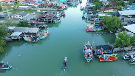 Steady-hovering-aerial-footage-of-a-fishing-village-revealing-fishing-boats,-people,-and-a-boat-moving-up-the-river