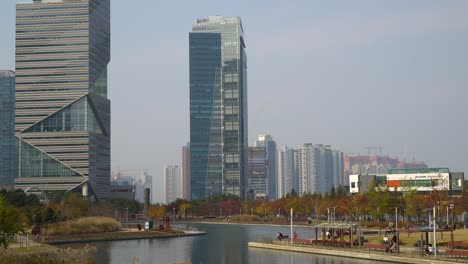 G-Tower-and-IBS-Tower-office-Buildings-Skyline-in-Incheon-Songdo-Central-Park-in-Autumn-with-People-Walking-near-the-Lake---aerial-static