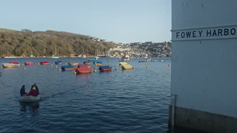 People-in-Motor-Boat-Return-to-Shore-from-Sail-Boats-Moored-in-of-Fowey-Harbour,-Cornwall,-England,-United-Kingdom---Slow-Zoom-out