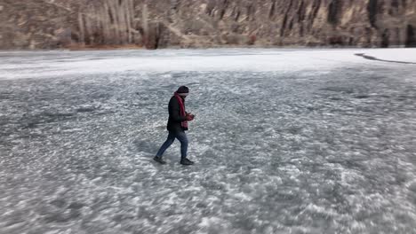 Aerial-Tracking-Shot-Of-Adult-Male-Walking-Across-Frozen-Khalti-Lake-And-Nearly-Slipping-Over