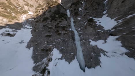 fpv-drone-flying-up-on-a-frozen-waterfall-at-an-austrian-mountain-in-spring-at-sunset