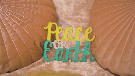 Cool-vintage-retro-shot-of-a-sign-saying-peace-on-earth-which-is-placed-on-a-couch-in-between-pink-orange-pillows-slow-motion-unique-scene