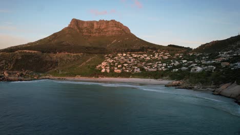 Table-Mountain-overlooking-Llandudno-Beach-at-sunset-in-Cape-Town,-aerial