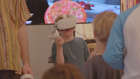 Young-boy-adjusting-Virtual-Reality-headset-while-other-kids-are-watching-him-in-a-classroom