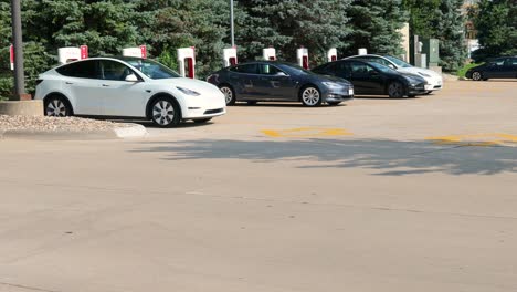 Tesla-Super-Charging-stations-in-a-parking-lot-for-a-grocery-store-and-restaurant-with-traffic-passing-by