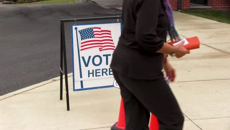 People-walk-by-vote-here-sign-with-American-flag-and-wheelchair-handicapped-friendly-signs