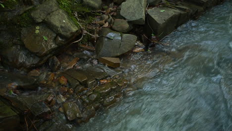 CLOSE-UP-of-a-fast-moving-creek-as-it-flows-along-a-rock-bank-in-the-forest