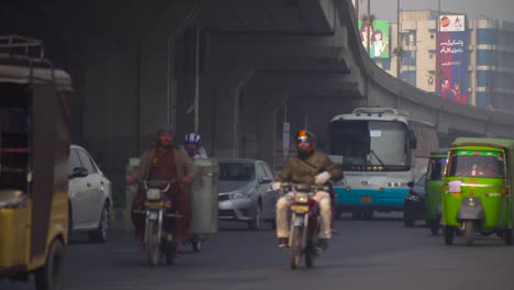 Traffic-close-up-at-the-road-under-the-fly-over,-passing-motor-bikes-and-cars,-Buses,-rickshaw`s,-Billboards-and-buildings-in-the-background