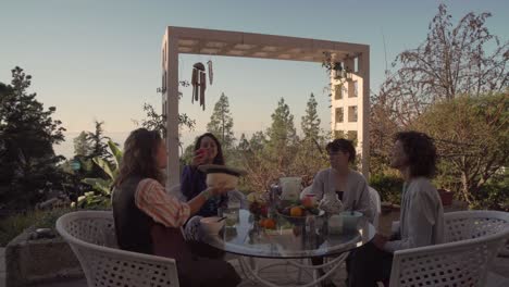 A-group-of-people-eating-at-an-outdoor-table,-smiling-and-having-fun-while-sharing-food
