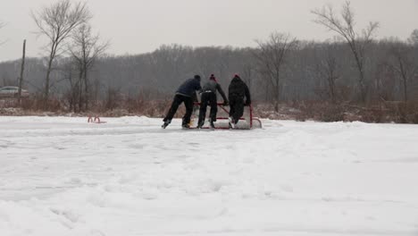 Three-teenagers-pushing-their-hockey-goal-to-remove-excess-snow-from-their-pond-hockey-field-while-it’s-still-snowing