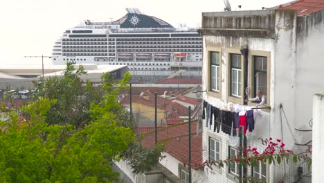 Portugiesische-Frau,-Die-Kleidung-Zum-Trocknen-Aus-Dem-Fenster-In-Lissabon-Vor-Dem-Hintergrund-Eines-Großen-Kreuzfahrtschiffes-Auslegt