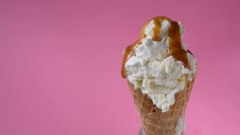 caramel-sauce-being-poured-over-vanilla-ice-cream-waffle-cone-on-fun-vibrant-pink-background