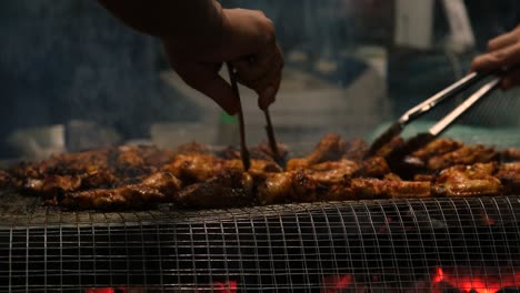 Closeup-View-of-Grilling-Chicken-Wings-on-BBQ-Grill-with-hands-holding-tongs