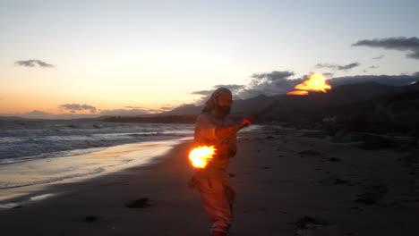 A-male-flow-art-dancer-in-silhouette-performing-his-fire-spinning-on-the-beach-at-sunset-with-ocean-waves-in-slow-motion