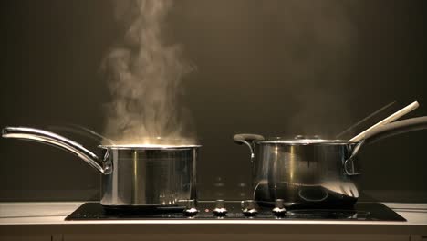 Tight-shot-of-a-pair-of-simmering-pans-on-a-cook-top-with-steam-rising-into-a-rangehood