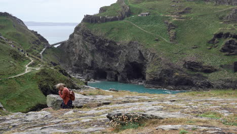 People-on-vacation-walking-on-top-of-a-cliff-along-the-path-that-leads-to-the-ruins-of-Tintagel-castle-and-bridge-to-the-island-in-Cornwall