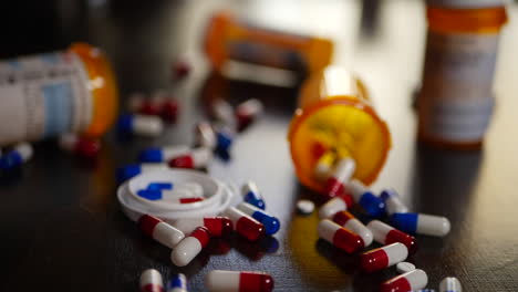 Many-prescription-pills-and-drug-capsules-spilling-onto-a-desk-with-orange-medicine-bottles-SLOW-MOTION