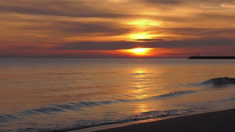 Sunrise-beach-view-with-calm-waves-and-glowing-sun-on-horizon,-mediterranean-coast-of-spain