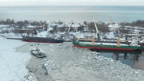 Cinematic-aerial-view-of-industrial-port-in-winter,-ships-surrounded-by-ice-floes