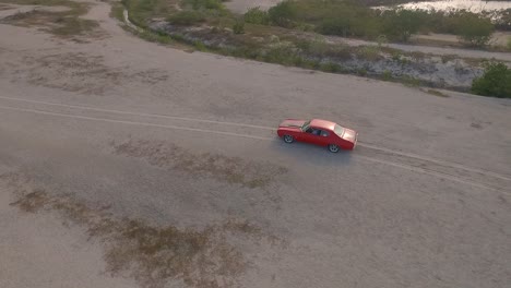 Drone-view-of-an-old-American-muscle-car-in-a-desert-during-a-sunset