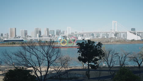 Rainbow-Bridge-Over-Tokyo-Bay-With-Olympic-Rings-Monument-On-A-Sunny-Day-In-Odaiba,-Minato,-Tokyo,-Japan
