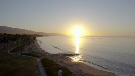 Santa-Barbara-Sunrise-looking-out-over-ocean-harbor-with-sailboats-palm-trees-and-running-path-on-beach-4k-Prores