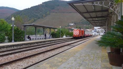 A-colorful-Portuguese-passenger-train-arrives-to-a-secluded-stop-in-a-mountainous-region-of-Portugal,-Caminhos-de-Ferro-Portugueses