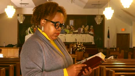 Young-black-lady-wearing-glasses-standing-in-empty-church-during-pandemic-reading-the-bible