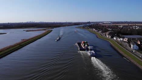 Vehicles-Driving-On-Riverbank-Road-With-Barges-Sailing-At-Noord-River-Near-Hendrik-Ido-Ambacht,-Netherlands