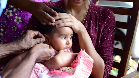Baby-girl's-ear-piercing-moment,-four-months-old-cute-baby-crying-while-the-mother-holds-her-tight