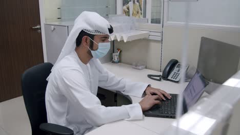 An-Arab-Man-Working-On-His-Laptop-In-The-Office---wide-shot