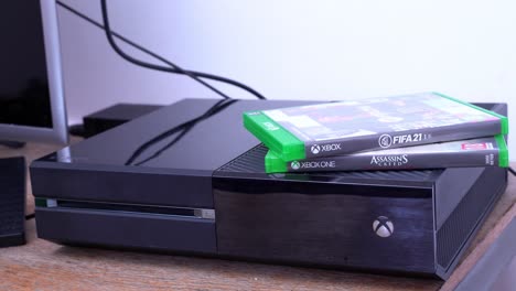 Consola-Xbox-One-Y-Juegos-En-Una-Mesa,-Zoom-De-Medio-A-Primer-Plano