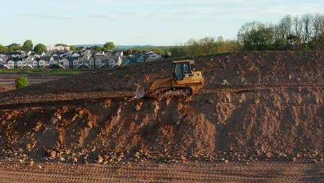Caterpillar-bulldozer-backs-up-mountain-of-dirt,-excavation-site