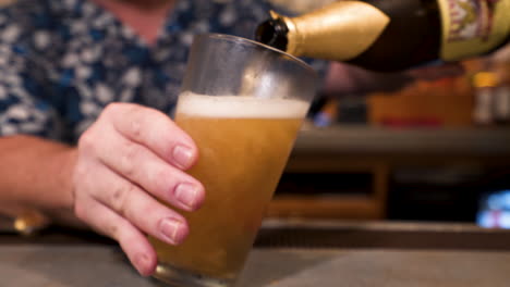 Bartender-heavily-pours-bottle-of-beer-into-frosted-pint-glass,-slider-slow-motion-HD