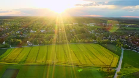 Flying-into-the-sun-with-a-drone-a-little-village-behind-a-rapeseed-feel-in-view-at-the-springtime