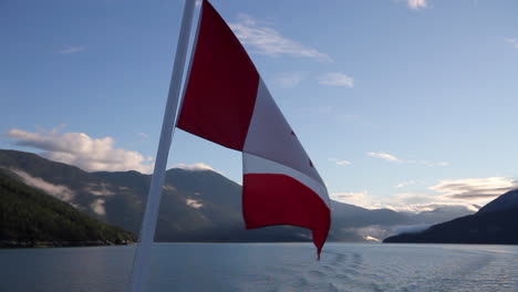 Canada-flag-on-ferry-against-morning-blue-sky-and-coastal-mountains