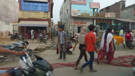 Gente-Que-Viaja-En-Motocicleta-A-Lo-Largo-De-La-Calle-En-Agra-Con-Gente-Comprando-En-Puestos-De-Mercado,-India