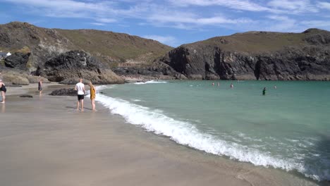 People-enjoying-the-blue-waters-on-summer-day-at-Kynance-Cove-in-Cornwall,-UK