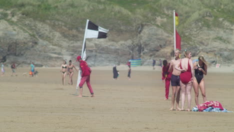 People-Wait-as-Lifeguards-Move-Beach-Safety-Zone-Flags,-Perranporth,-Cornwall,-England,-telephoto