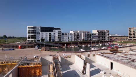 Backwards-aerial-movement-showing-construction-site-of-luxury-apartment-Kade-Zuid-complex-being-build-in-former-industrial-area-with-finished-Kade-Noord-behind-recreational-port-in-the-background