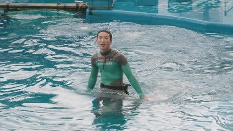 Delphintrainer-Winkt-Dem-Publikum-Zu,-Während-Er-Auf-Einem-Großen-Tümmler-Reitet,-Der-Im-Pool-Des-Umino-mori-aquariums-In-Sendai,-Miyagi,-Japan,-Schwimmt