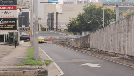 A-rear-view-of-a-yellow-taxi-as-it-travels-slowly-away-down-a-quiet-urban-road,-as-the-vehicle-reaches-the-bottom-of-the-street-it-turns-off-and-drives-out-of-sight,-Panama-City