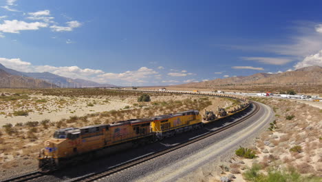 Aerial-view-of-train-carrying-hundreds-of-US-military-vehicles,-tanks-and-humvees-are-transported-by-railway-through-the-desert-outside-Palm-Springs