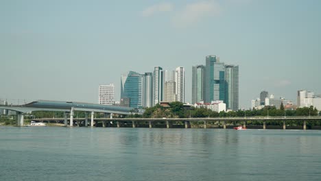 Water-Rescue-Unit-Motorboat-Moves-with-Speed-at-Han-river-with-Seoul-Skyline,-Dangsan-Railroad-Bridge,-Traffic-on-Gangbyeon-Express-Way,-Mecenatpolis,-SEAH-Tower,-KB-Insurance,-riverfront-landscape