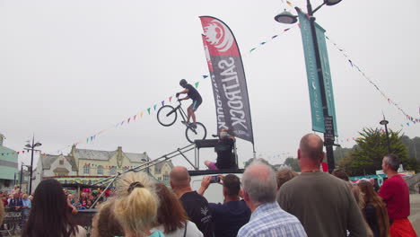 Man-Performs-Dangerous-Stunt-On-A-Mountain-Bike-In-Truro,-Cornwall,-England-With-Audience-Watching