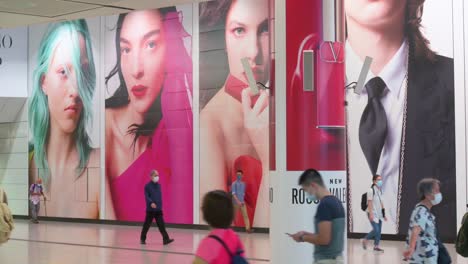 Commuters-wearing-protective-masks-walk-past-a-large-commercial-advertisement-banner-at-Hong-Kong-MTR-subway-station-early-morning-in-Central-district,-Hong-Kong